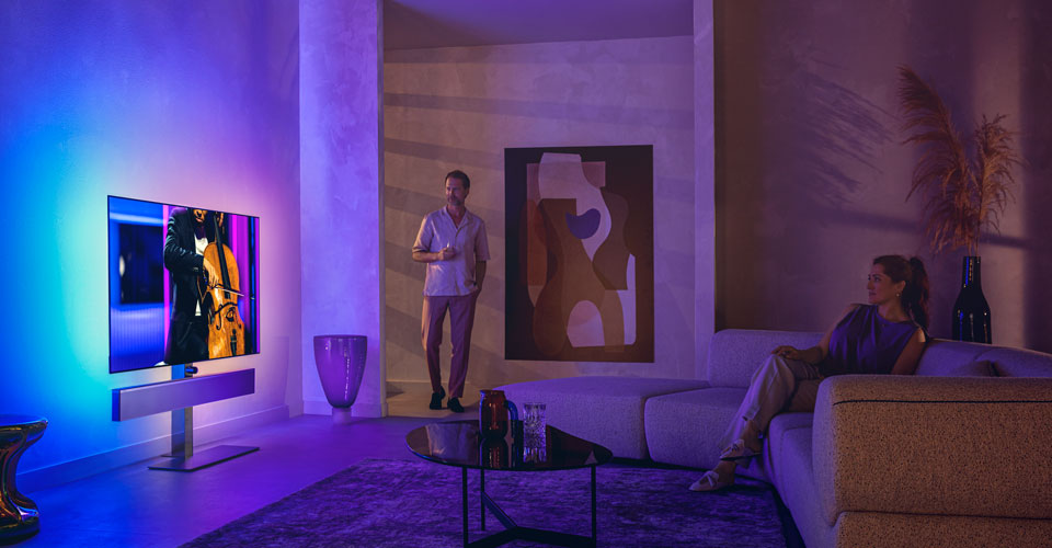 Mann og kvinne i en stilig stue som ser p&aring; en Philips Ambilight-TV som viser en celloopptreden